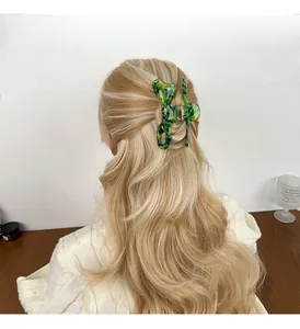 Detail shot of a large green marble acetate bow hair claw clip worn on wavy brown hair