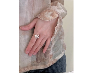 Detail shot of a delicate gold ring with a white pearl flower design worn on finger