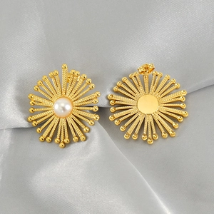 Golden sunburst geometric earrings with pearls on a grey silk fabric background