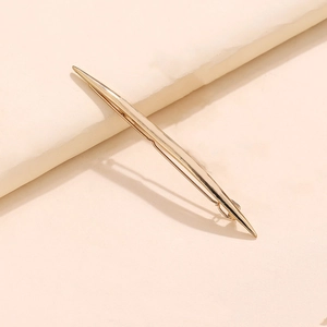 Golden alloy streamlined geometric V-shaped hair clip set on a soft pink surface