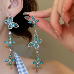 Close-up of dangling butterfly and flower earrings with blue rhinestones on a model