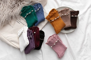 Detail of knit socks showing pearl embellishments and ruffled cuffs in various colors