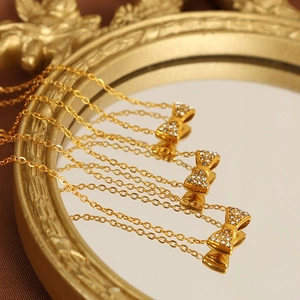 Collier à nœud doré chic avec cristaux pavés sur une surface de miroir vintage