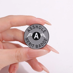 Runde Asshole Merit Badge Emaille-Anstecknadel mit weißen Flügeln in der Hand gehalten