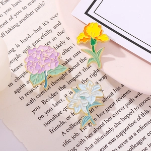 Three-piece floral enamel pin set with violet, lily, and iris on an open book background