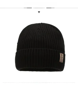 Detail of black ribbed knit beanie with brown leather logo patch and textured finish