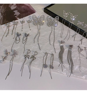 Detailed close-up of silver bow and heart tassel earrings with sparkling rhinestones
