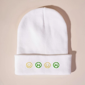 Close-up of white knit beanie featuring four embroidered emoji faces and soft texture