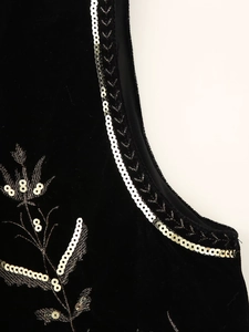Detailed close-up of silver sequins and leaf embroidery on black velvet fabric vest
