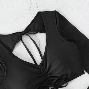 Detail of black V-neck swimwear top with ruched bust and ties on white textured wall