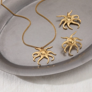 Golden octopus necklace and earrings set displayed on a grey tray with soft lighting