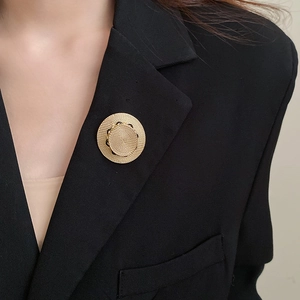 Detail einer goldenen runden Brosche mit Struktur auf einem schwarzen Sakko-Revers