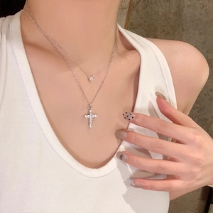 Detail shot of a silver layered necklace featuring a sparkling cross pendant and moissanite