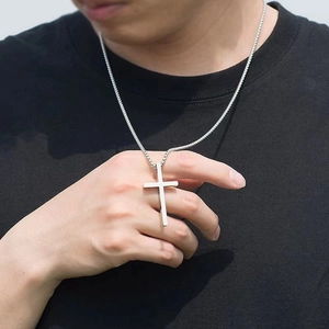 Close-up of a silver cross pendant necklace with a fine chain worn by a male model