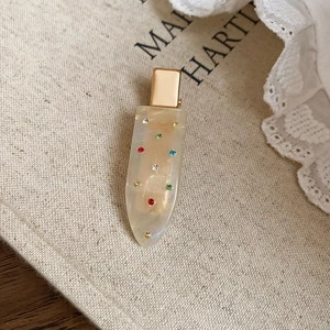 Macro detail of cream resin hair clip with colorful rhinestones on beige canvas background