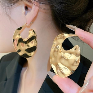 Detailed macro view of large chunky gold irregular geometric earrings with wavy metallic finish