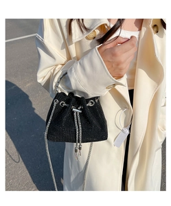 Detail of a mini black rhinestone bucket bag with silver chain strap on a trench coat