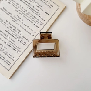 Square amber hair claw clip with spring and teeth on a white book aesthetic background