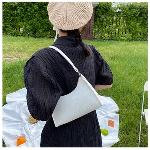 Detailed view of a white crocodile pattern underarm bag shown in an outdoor lifestyle setting