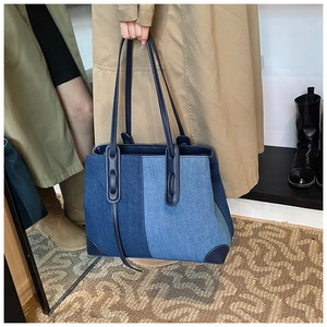 Detailed view of large denim tote bag featuring contrast colors and dark blue leather handles
