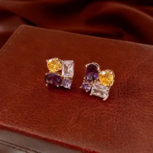 Elegant gold oval earrings with multicolored zircons on a luxury brown leather surface