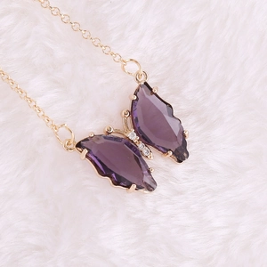 Detail of a golden necklace featuring a purple butterfly pendant with crystal cut wings