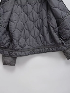 Detailed close-up of charcoal grey quilted jacket with gourd pattern stitching and piping