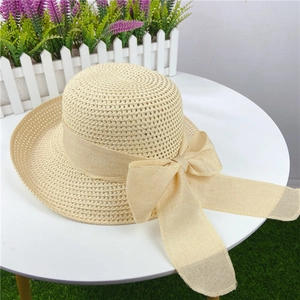 Detail of woven straw sun hat featuring a large elegant ribbon bow on white tabletop