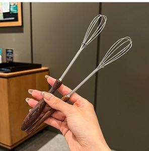 Detail of two mini spring whisks with dark brown wooden handles and stainless steel coils