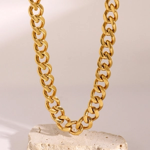 Close-up of gold chunky chain necklace draped over a textured beige stone base