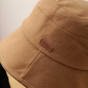 Classic tan fabric bucket hat with a brown leather patch detail and fine textile texture