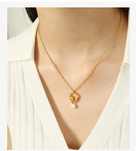 Detailed close-up of a golden pendant with a white pearl on a gold necklace worn by a model