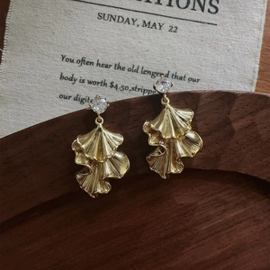 Detailed view of gold textured ginkgo leaf earrings with a sparkling zircon stud on wood