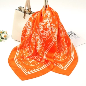 Detail of orange paisley silk scarf tied to a cream handbag with floral patterns