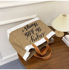 Detail of jute and canvas tote bag with black cursive text on a dark wooden table