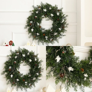 Christmas wreath with green pine needles, pine cones, and red berries on a white wall