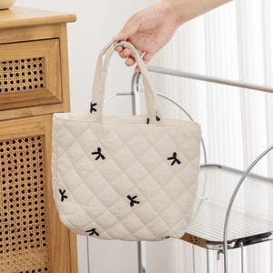 Detail of cream quilted tote bag featuring black embroidered bows and soft fabric texture
