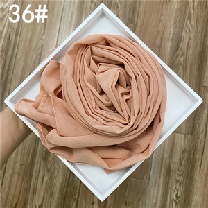 Détail du foulard en mousseline rose abricot avec paillettes dorées sur plateau blanc