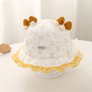 Détail d'un chapeau de soleil bébé avec volant à carreaux jaunes et motif cerise