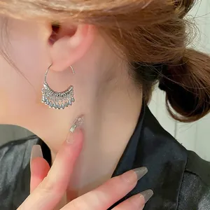Silver C-shaped hoop earrings with metallic tassel teardrops worn by a model