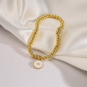 Detail of 4mm gold beaded bracelet with Fé engraved white enamel charm on silk fabric