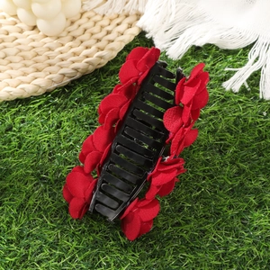 Detail of black plastic hair claw clip with red flocked fabric rose flowers on green grass