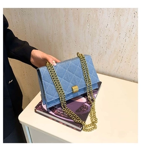 Close-up of blue denim quilted bag with golden chain strap on a coffee magazine