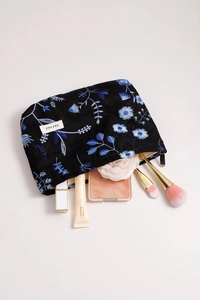 Detail of floral embroidery on black linen makeup bag with silver zipper and cosmetic items