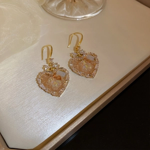 Detailed close-up of heart-shaped gold earring with teddy bear and sparkling zircon stones