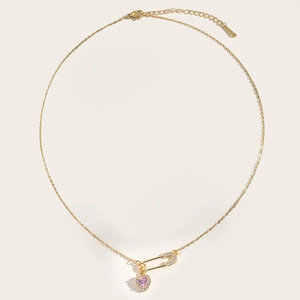Detailed close-up of a gold safety pin necklace with a sparkling pink heart pendant