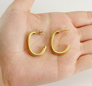 Detailed macro view of 18k gold C-shaped earrings with textured ribbed metal pattern