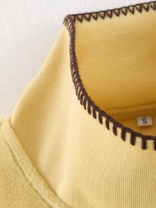 Detail view of yellow wool-like cape neckline with brown whipstitch trim and size S label