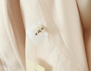 Dettaglio ravvicinato dell'etichetta e della fodera beige del cappotto lungo sfiancato
