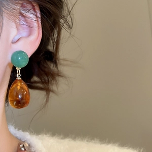 Macro view of gold droplet earring with green bead and amber resin pendant on model